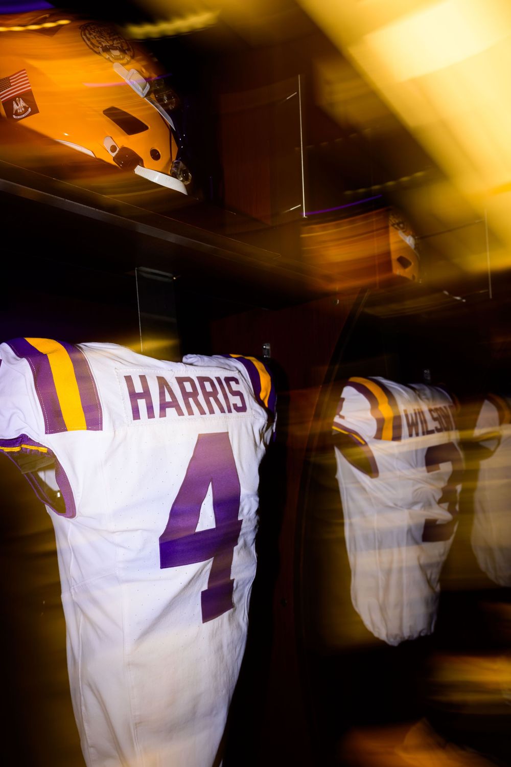 White football jersey with purple and gold trim, number 4 and name Harris, hanging in a locker beside a gold helmet and another jersey.