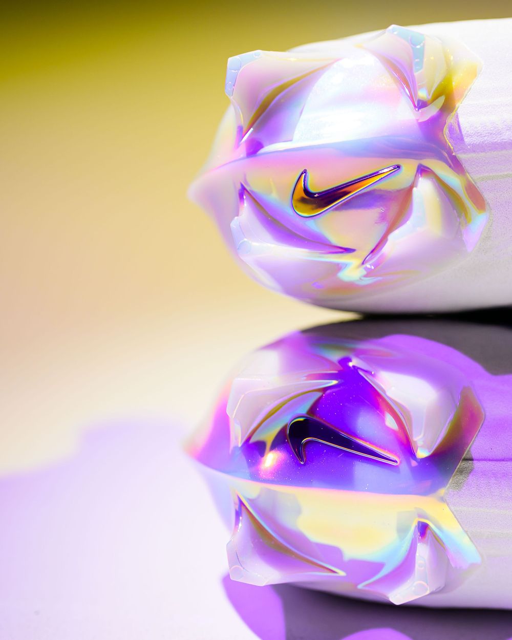 Close-up of iridescent holographic Nike shoe toes with gold swoosh logos, reflecting purple and yellow light on a glossy surface.