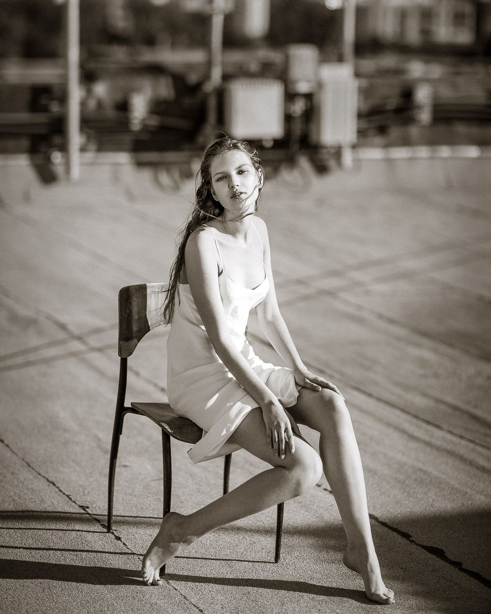 Young woman in white dress seated on chair outdoors, black and white portrait photography.