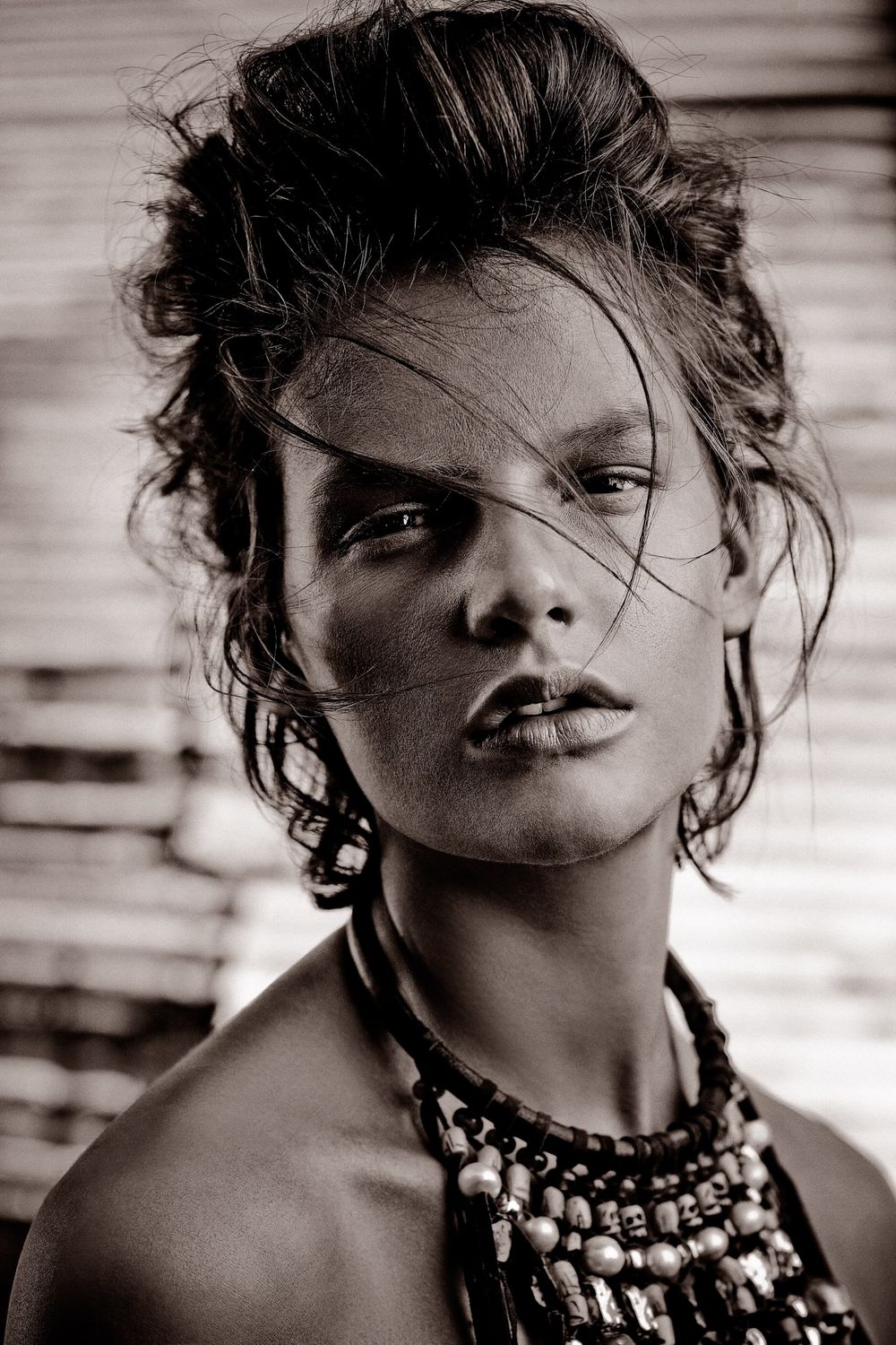Black and white portrait of a young woman with updo hair, beaded necklace, and a strand of hair across her face.