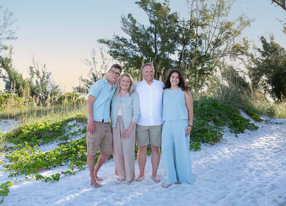 Family in soft blue and white posing among sea oats on the dunes at sunset
