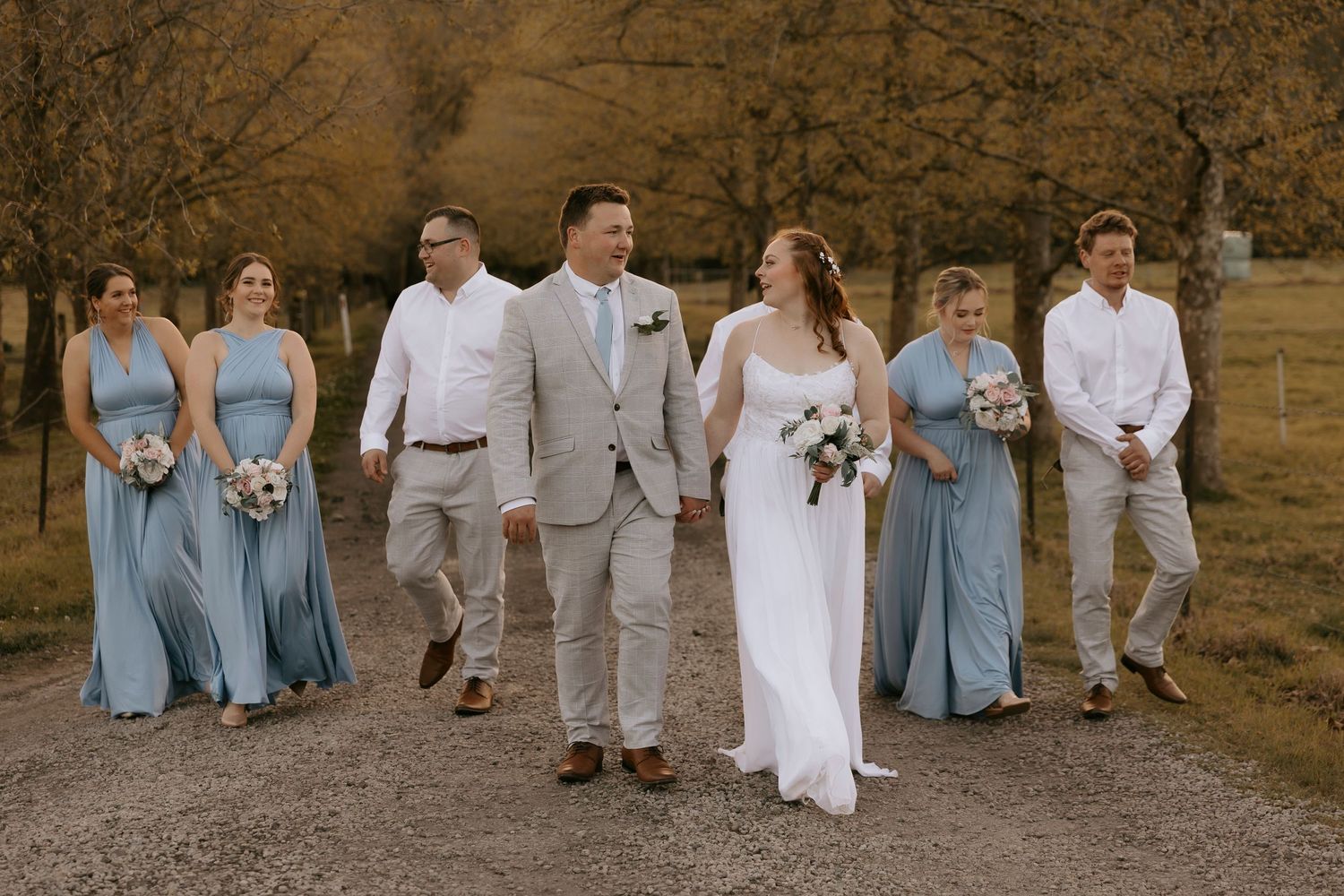 Wedding party posing against rustic brick wall in light blue and beige attire.