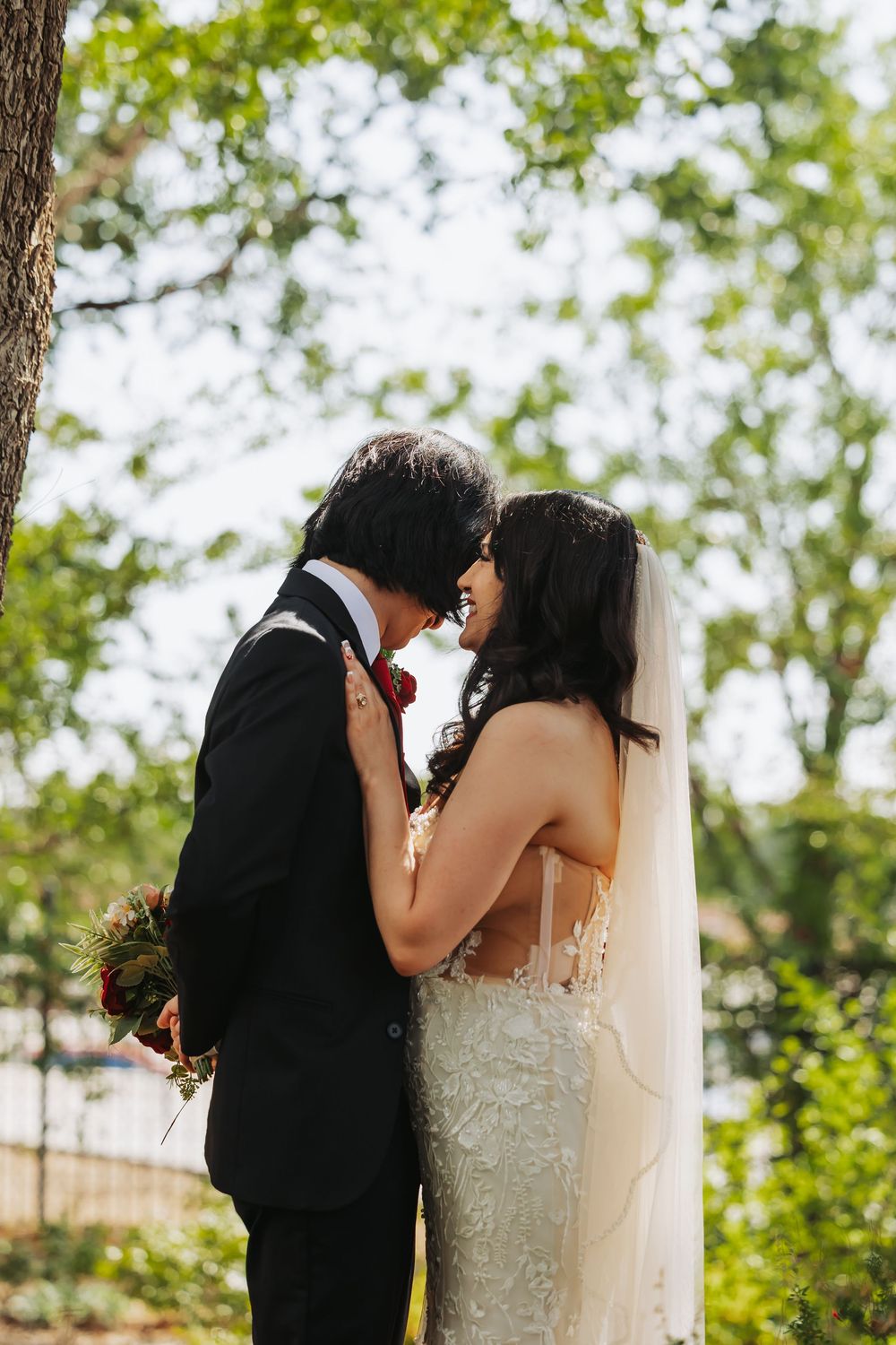 A bride and groom share a romantic moment outdoors, surrounded by lush green trees on their wedding day.