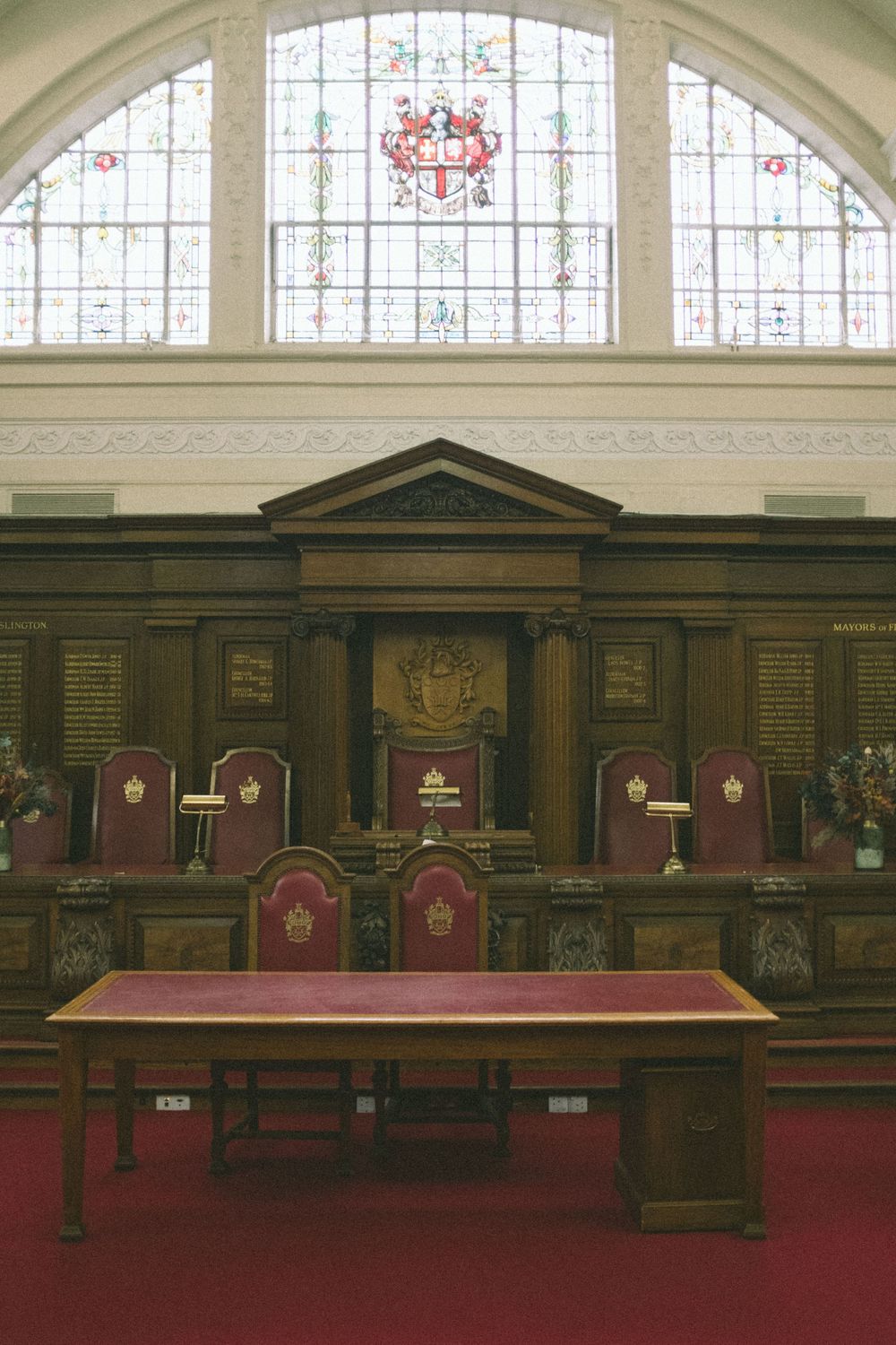 Ornate Islington Town Hall interior with red velvet judges chairs, wooden paneling, stained glass window, and red carpet.