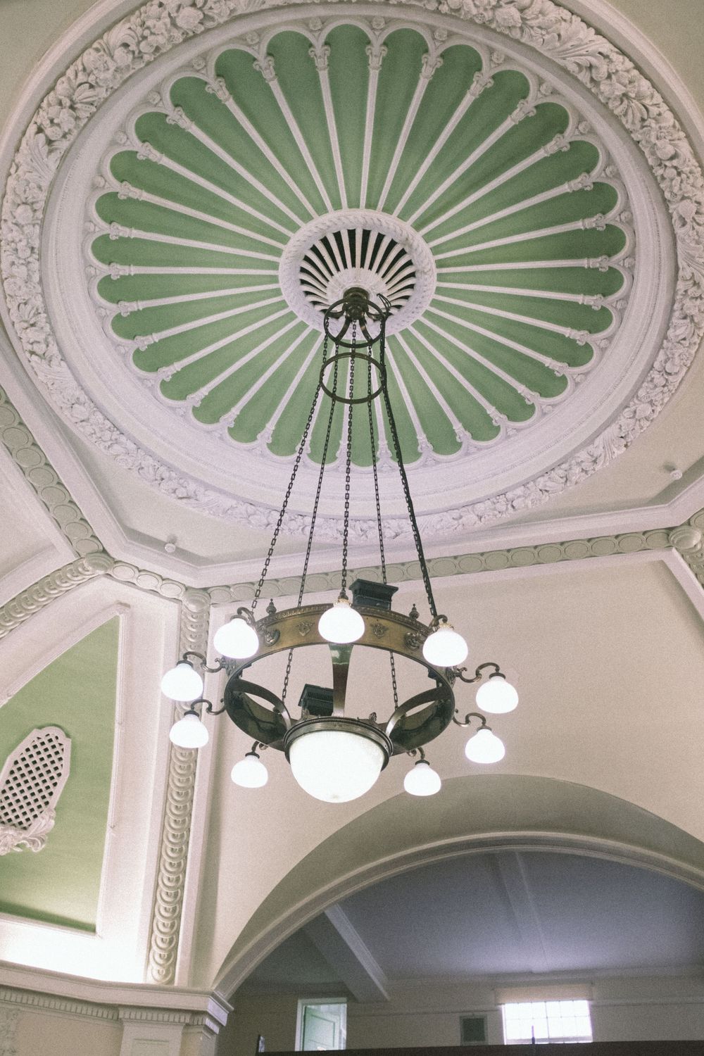 Ornate green and white ceiling dome with decorative plasterwork and vintage chandelier in an elegant historic building.