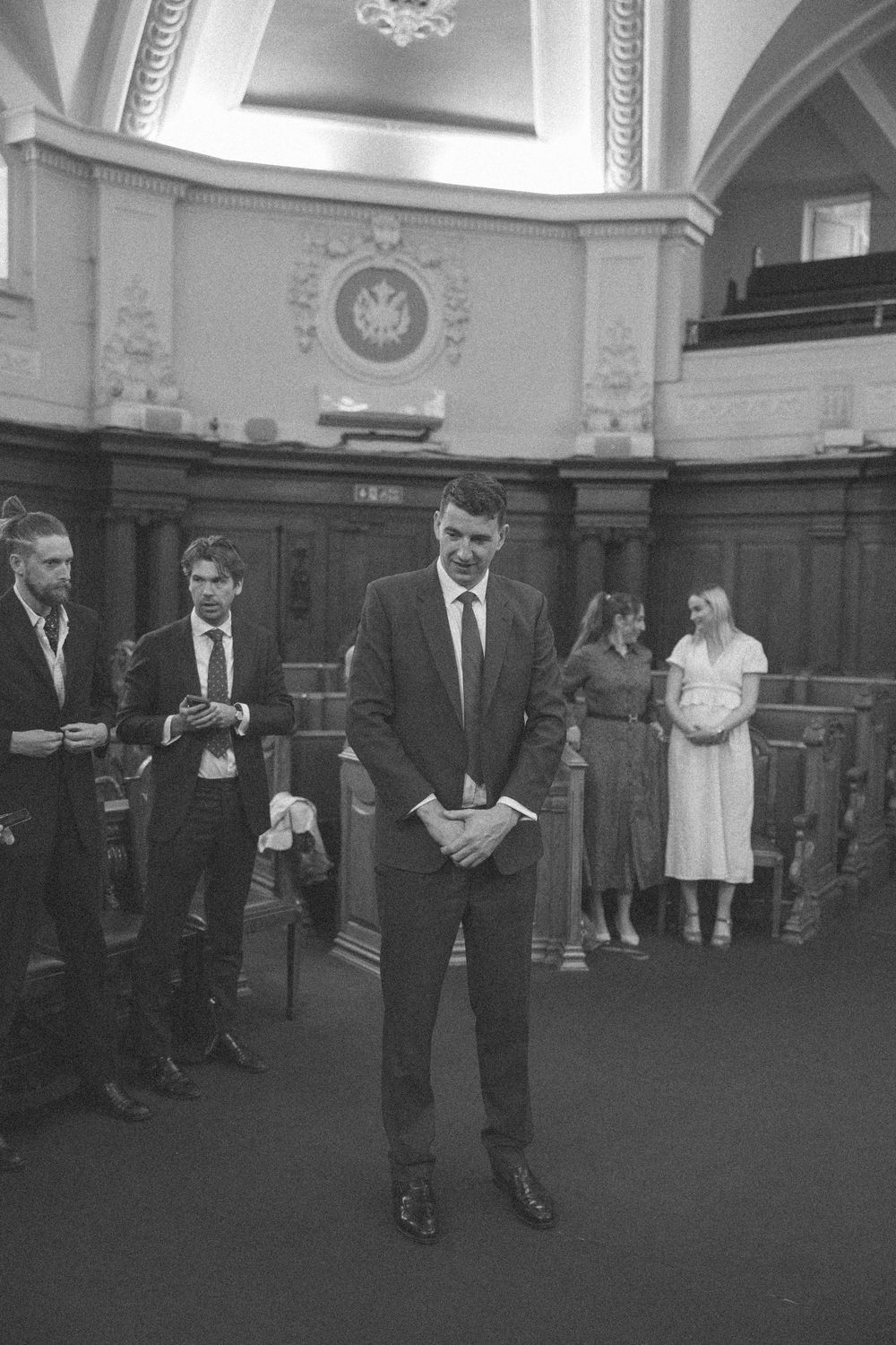 Black and white photo of a man in a suit standing in a grand hall during a formal ceremony.