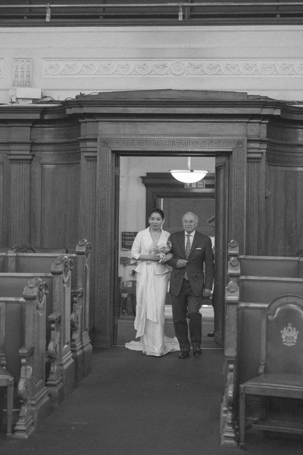 Black and white photo of a bride in a white gown walking down the aisle.