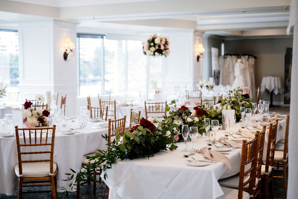 Elegant wedding reception hall with white-draped tables, wooden chairs, floral centerpieces and bright windows Stamford Plaza Queensland