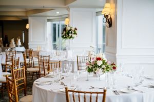 Elegant banquet hall with round tables, white linens, floral centerpieces, and wooden chiavari chairs set for a wedding reception Brisbane
