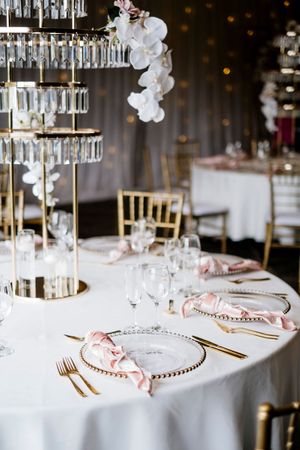 Elegant wedding reception table with gold-rimmed glass chargers, pink napkins, crystal tiered centerpiece and white orchids Stamford Plaza
