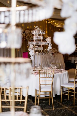 Elegant wedding reception with gold chiavari chairs, a tiered crystal centerpiece, white floral arrangements and warm string lights Brisbane