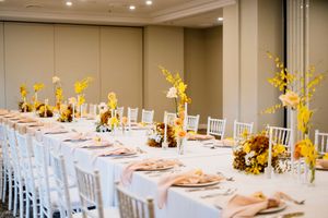 Elegant wedding reception hall with long white tables, blush napkins, and yellow and white floral centerpieces in a bright, modern venue