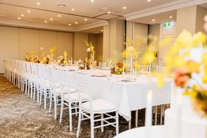Elegant banquet hall with long white-draped tables, white chairs, and yellow floral centerpieces set for a wedding reception Stamford Plaza
