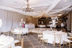 Elegant banquet hall set for a wedding reception with round white-linen tables, gold chiavari chairs, a chandelier and draped white fabric