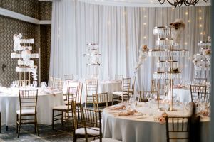 Elegant wedding reception hall with round tables, gold chiavari chairs, white linens, tall crystal centerpieces and draped ceiling fabric