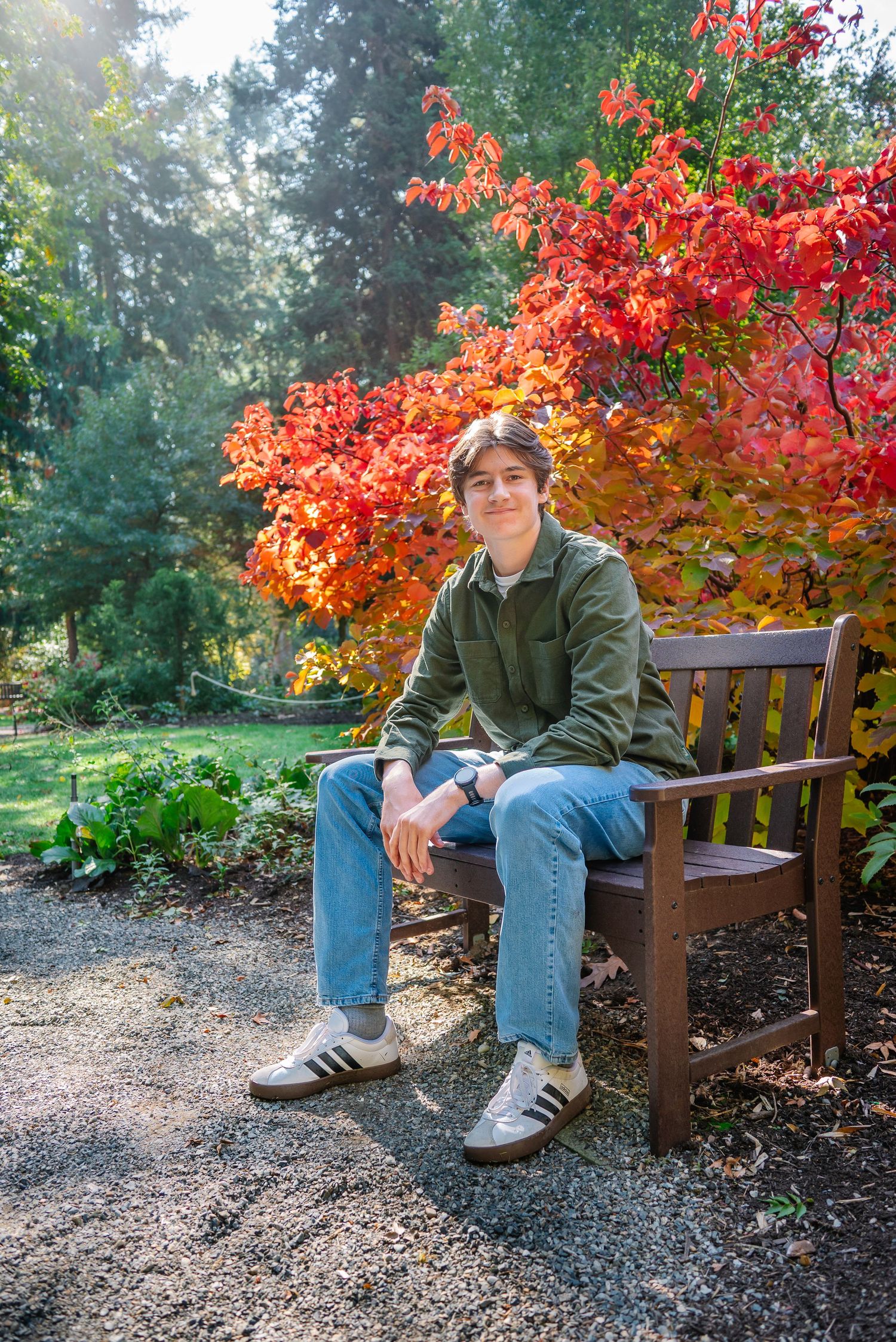 Senior seated on a wooden bench beside vivid autumn foliage and garden greenery