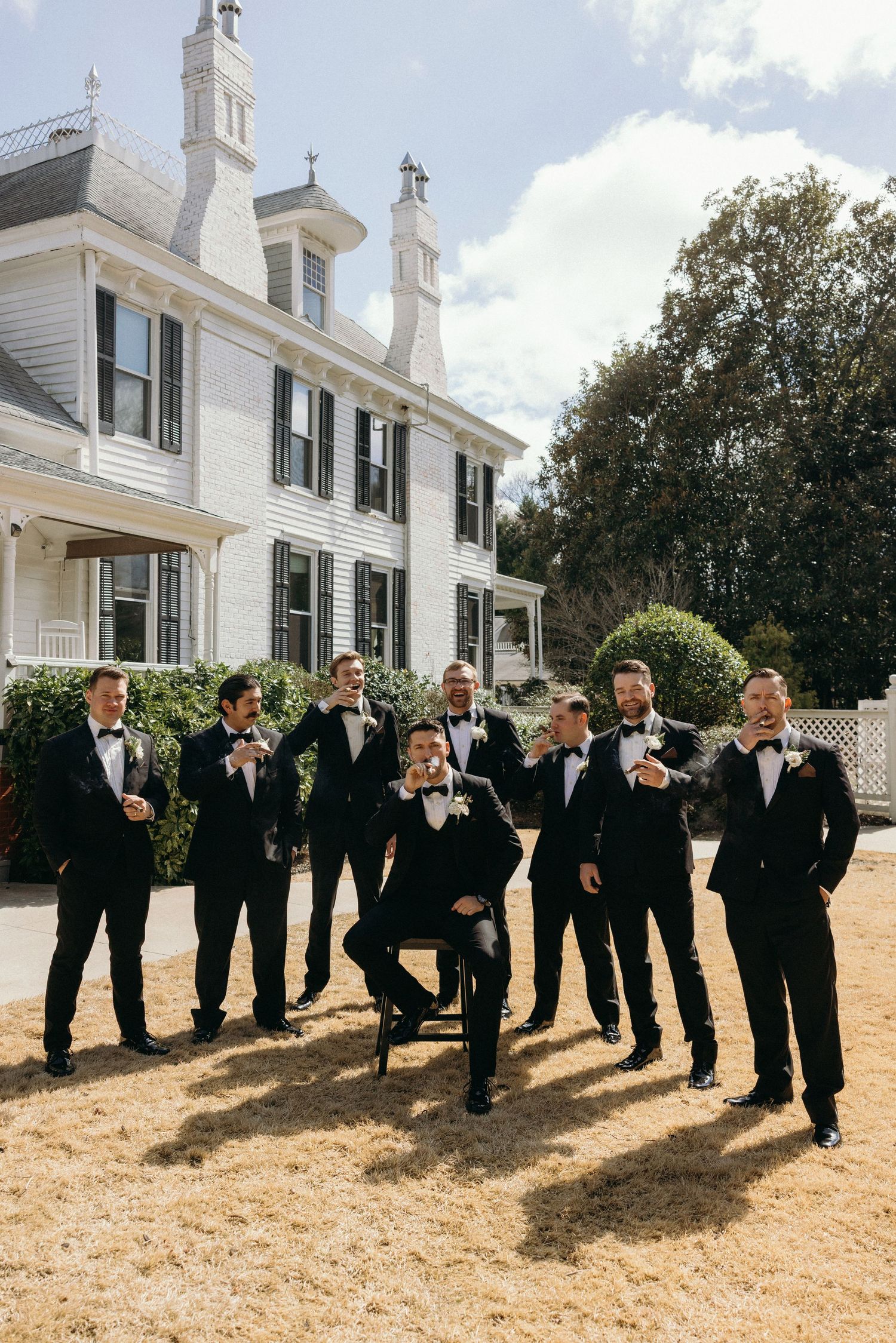 Groomsmen in black tuxedos with bow ties pose outside The Wildflower 301.