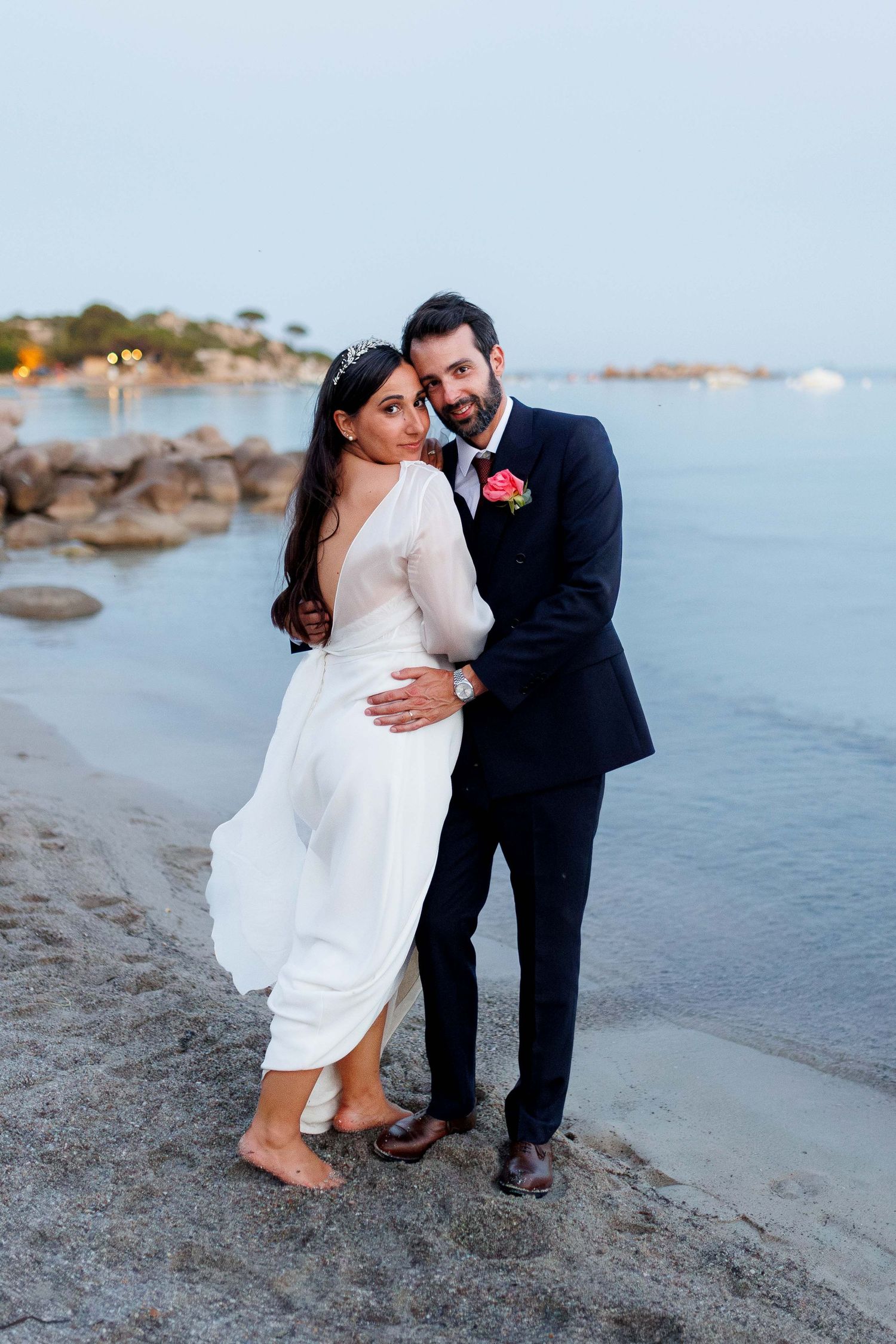 Bride and groom walking hand in hand on a wooden pier by the sea, wearing sunglasses on their wedding day.
