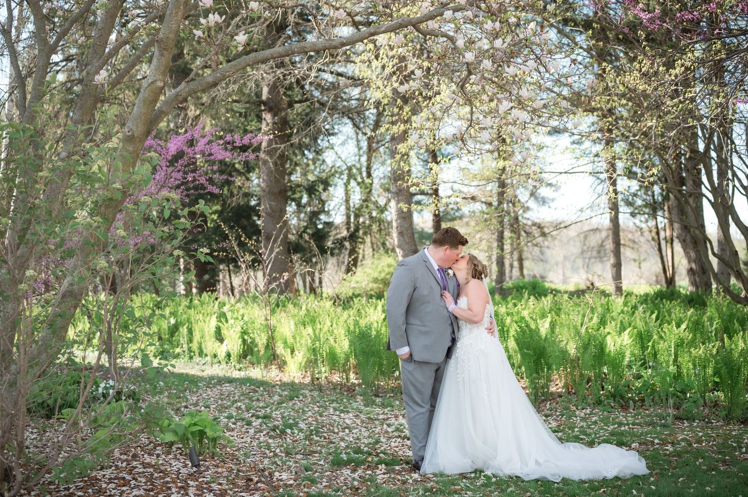 Bride and groom share an intimate moment, touching foreheads, at an outdoor vineyard wedding with stone pillars and green fields.