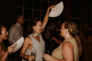 Women dancing and holding white hand fans at an elegant evening party or wedding reception celebration.
