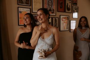 Bride in white gown laughs joyfully with bridesmaids in black and silver dresses before wedding ceremony.