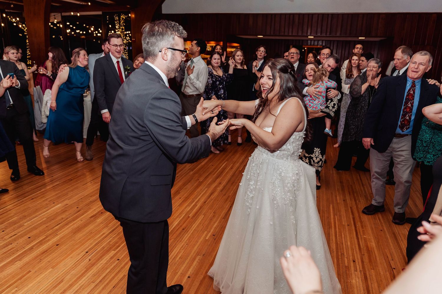 Bride and groom share a romantic first dance surrounded by cheering wedding guests in an elegant ballroom.