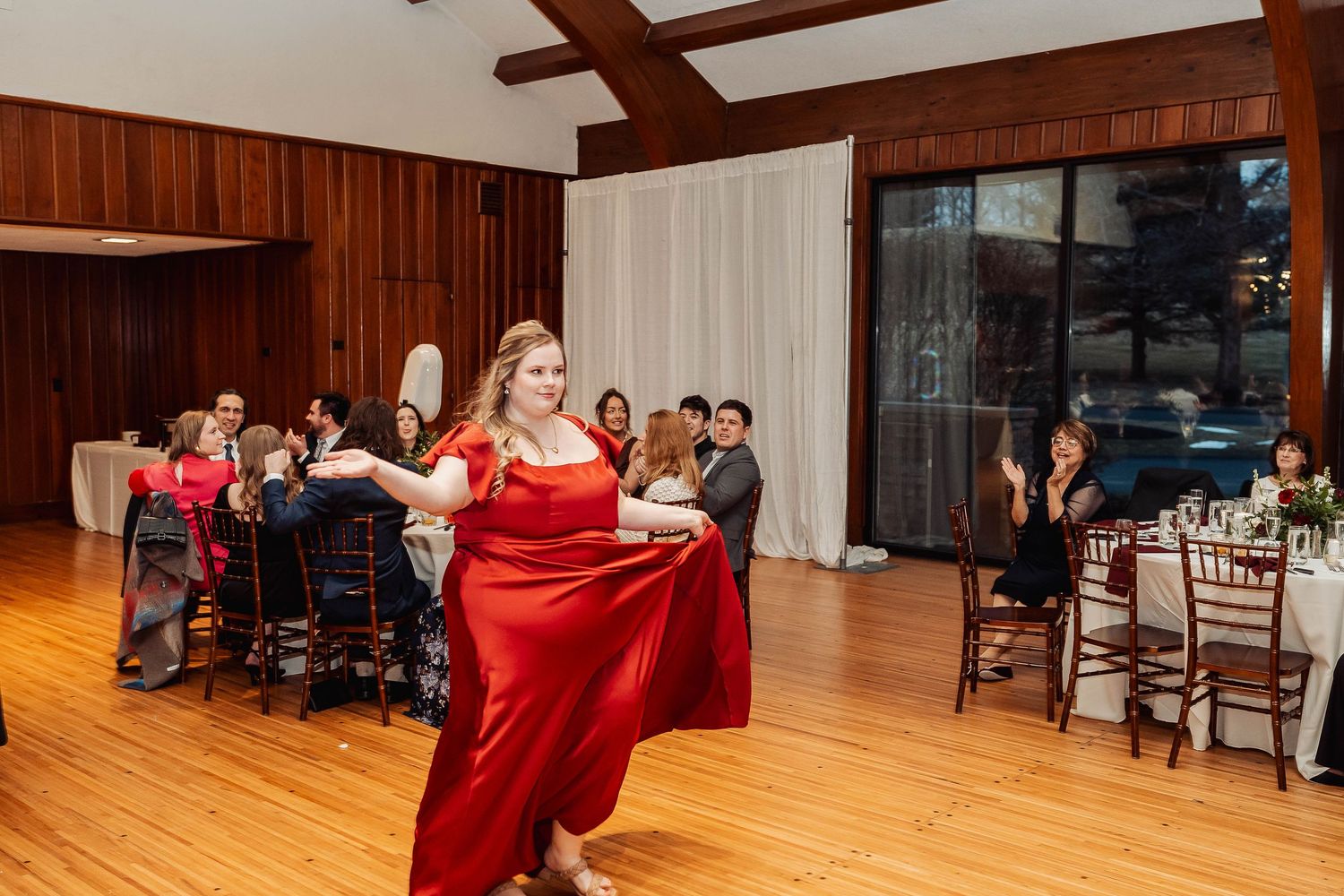 Woman in red dress dancing gracefully at an elegant indoor wedding reception with guests seated at tables.