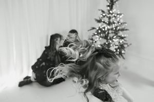 Black and white photo of children playing near a decorated Christmas tree with bokeh lights.