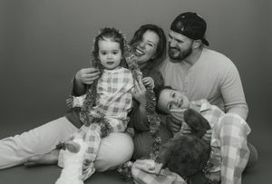 Black and white family photo with parents and two young children laughing together with festive tinsel garland.