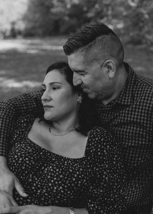 A black and white portrait of a couple embracing outdoors, the man in a checked shirt leaning gently against the woman's head.