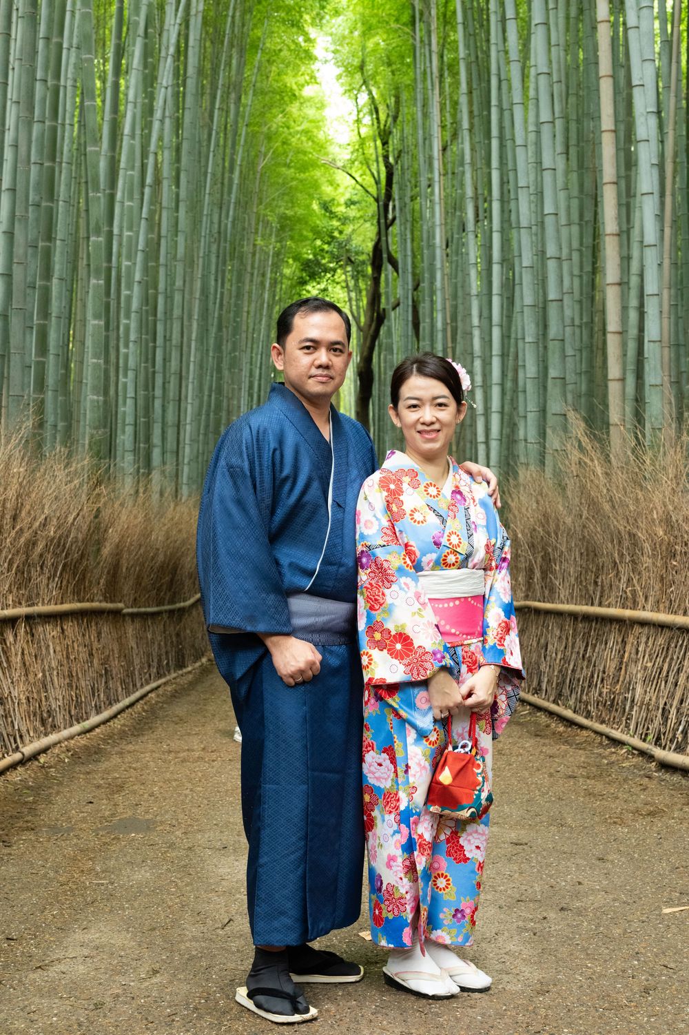 Couple in traditional Japanese kimono and yukata posing on a path through the towering green Arashiyama bamboo grove in Kyoto, Japan.