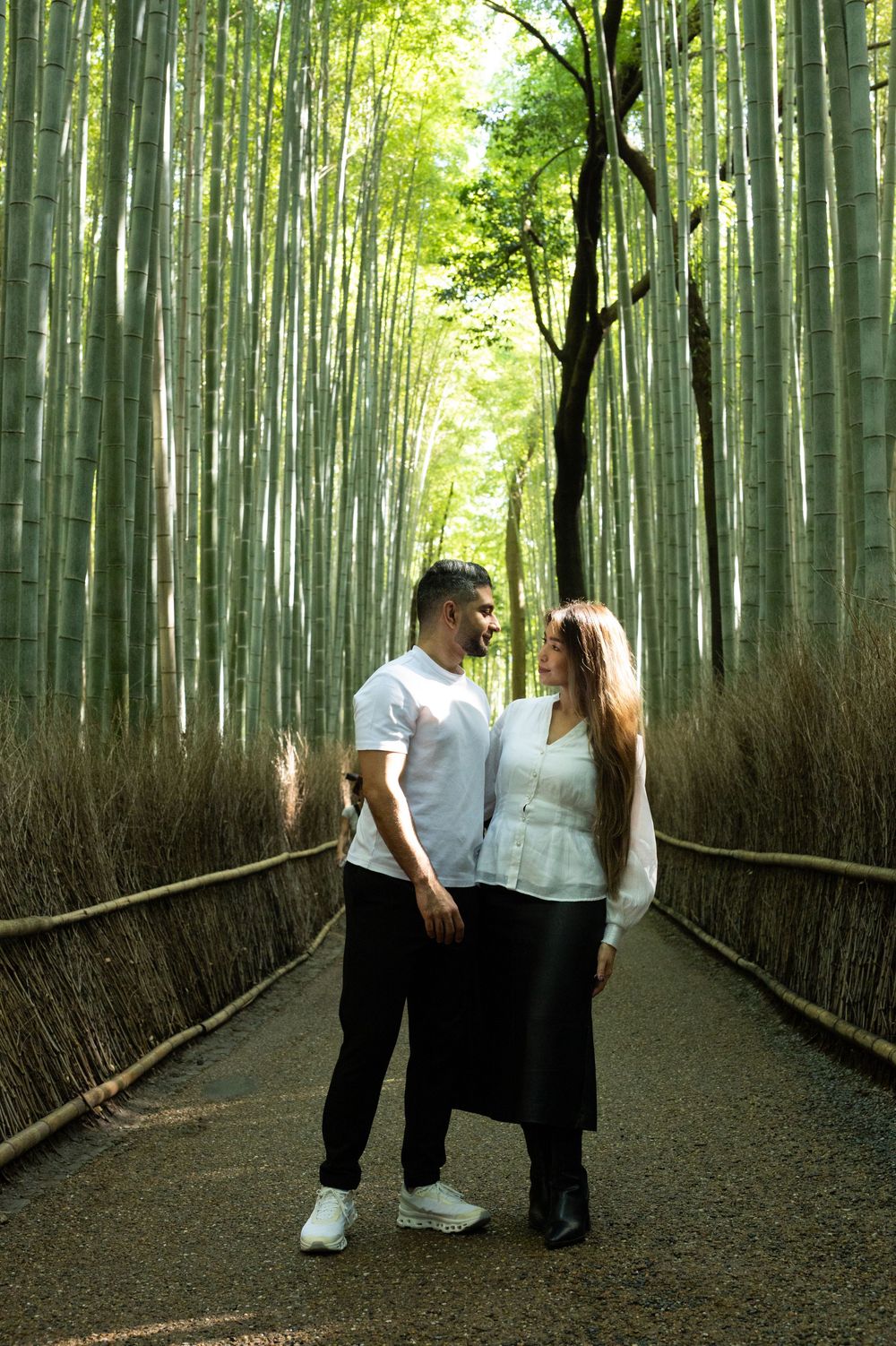 Couple in white tops embracing on a path through the towering green bamboo forest in Arashiyama, Kyoto, Japan.