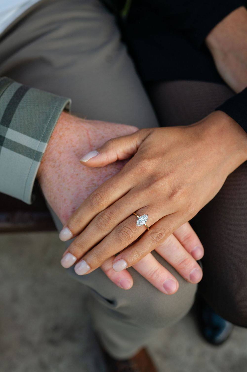 Woman's hand with a marquise diamond engagement ring resting on an older man's hand, seated together on a bench.