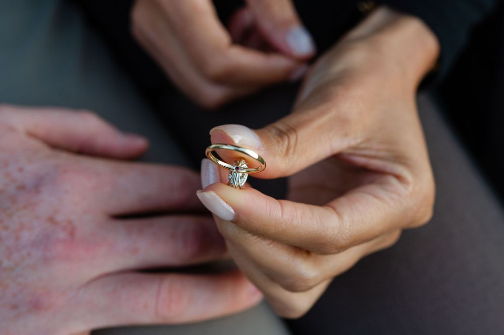 Close-up of a woman's hands holding a gold solitaire diamond engagement ring beside a man's hand.