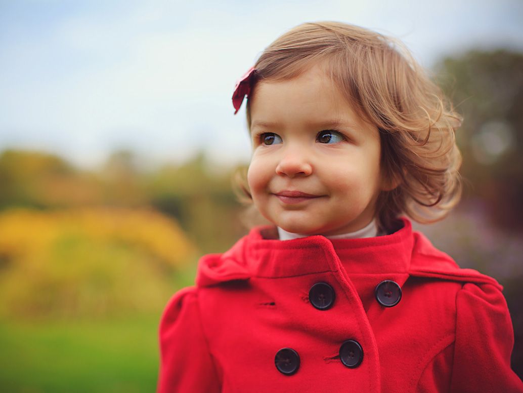 Portrait of toddler girl in red peacoat with mischievous smile at botanical gardens by Brighton, MI photographer
