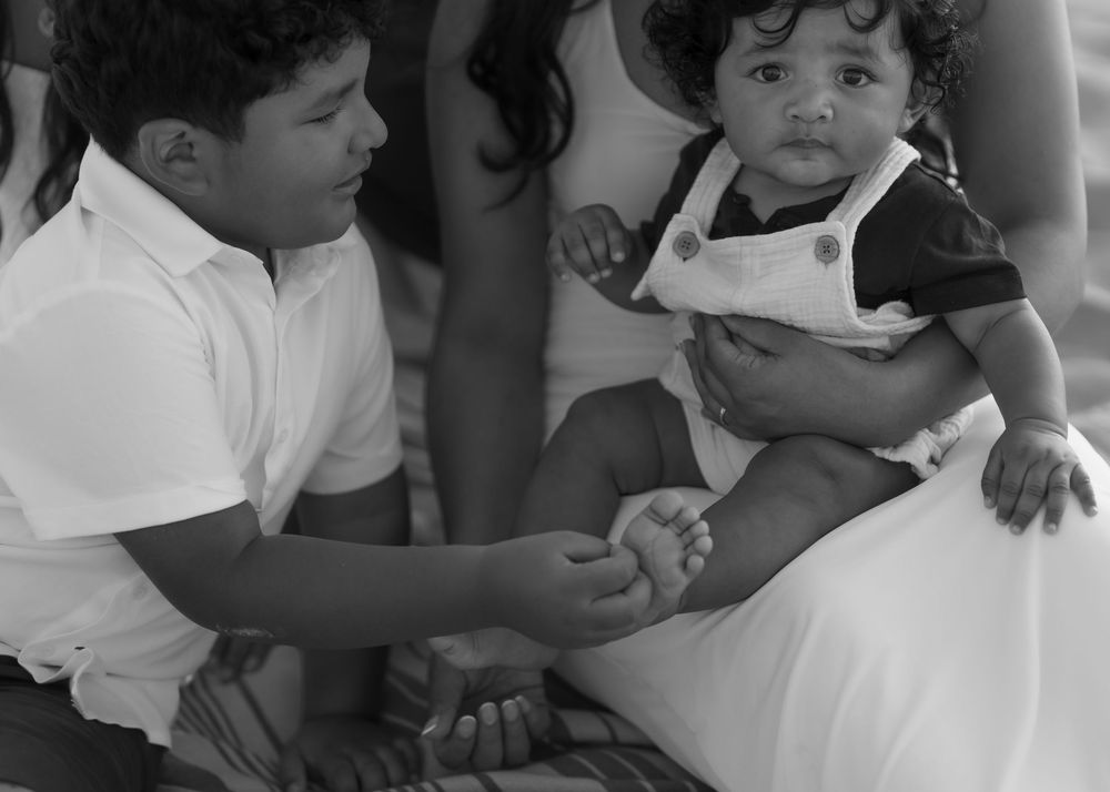 Black and white photo of a young boy interacting with a toddler in overalls held by an adult.