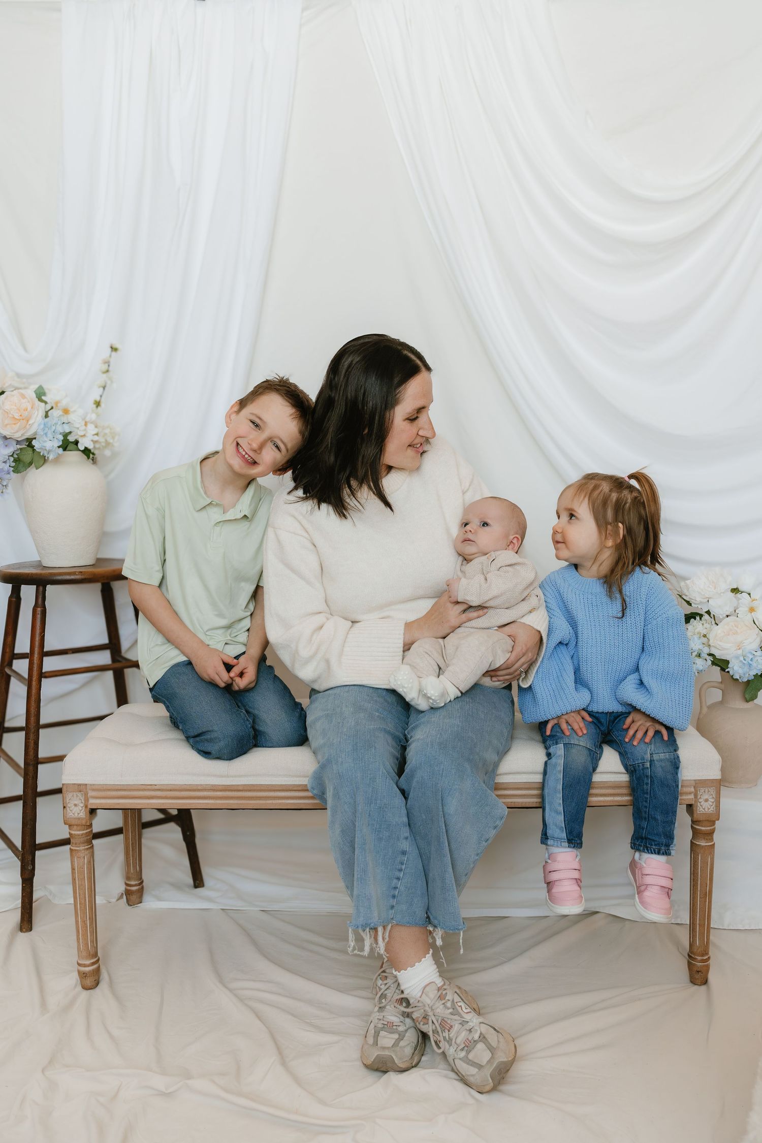 Mother sits on a bench with three children, including a baby, in a bright white studio setting in Halifax, Nova Scotia.