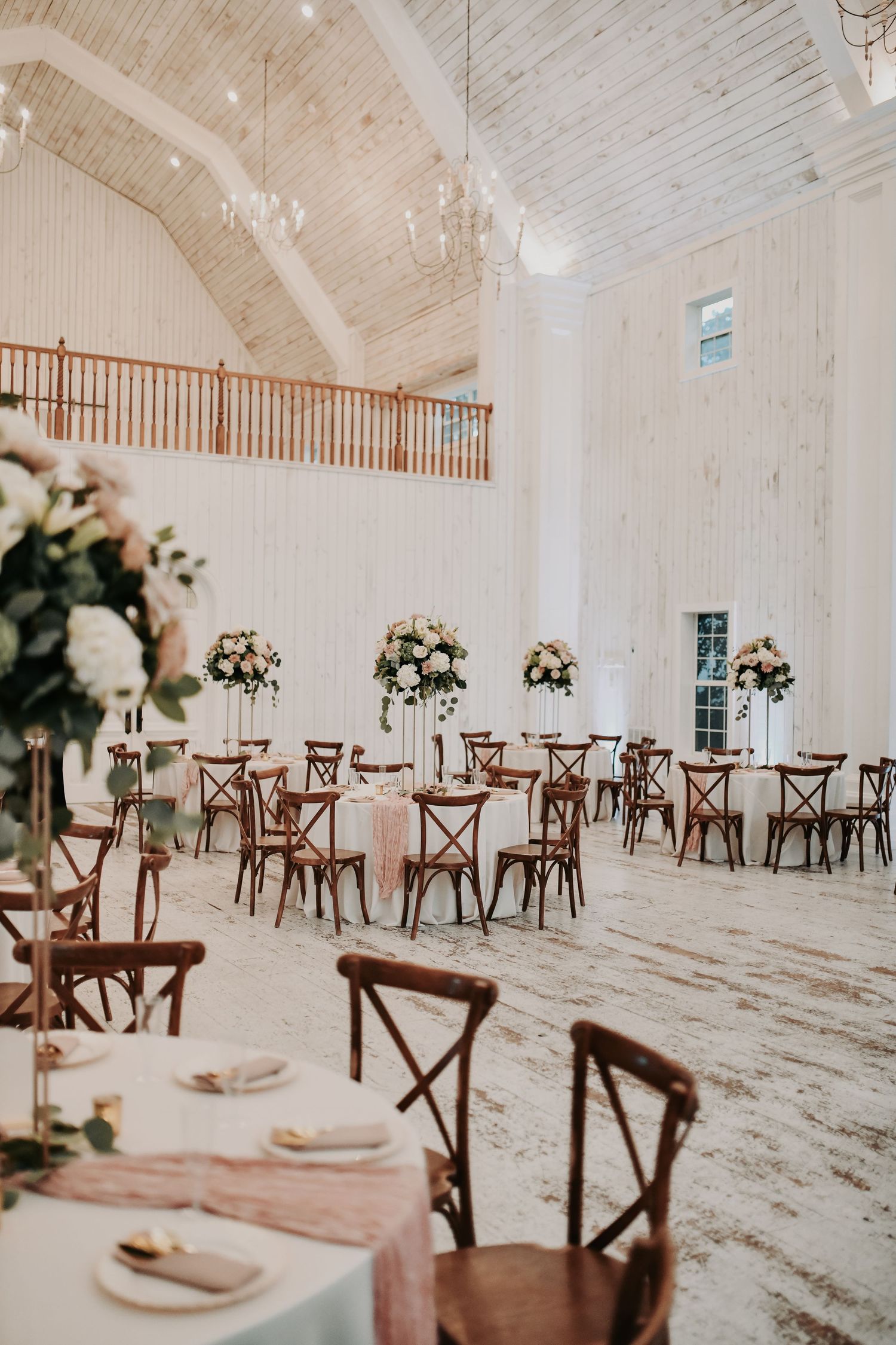 Bright white wedding reception with high arched ceilings and rustic wooden farmhouse chairs