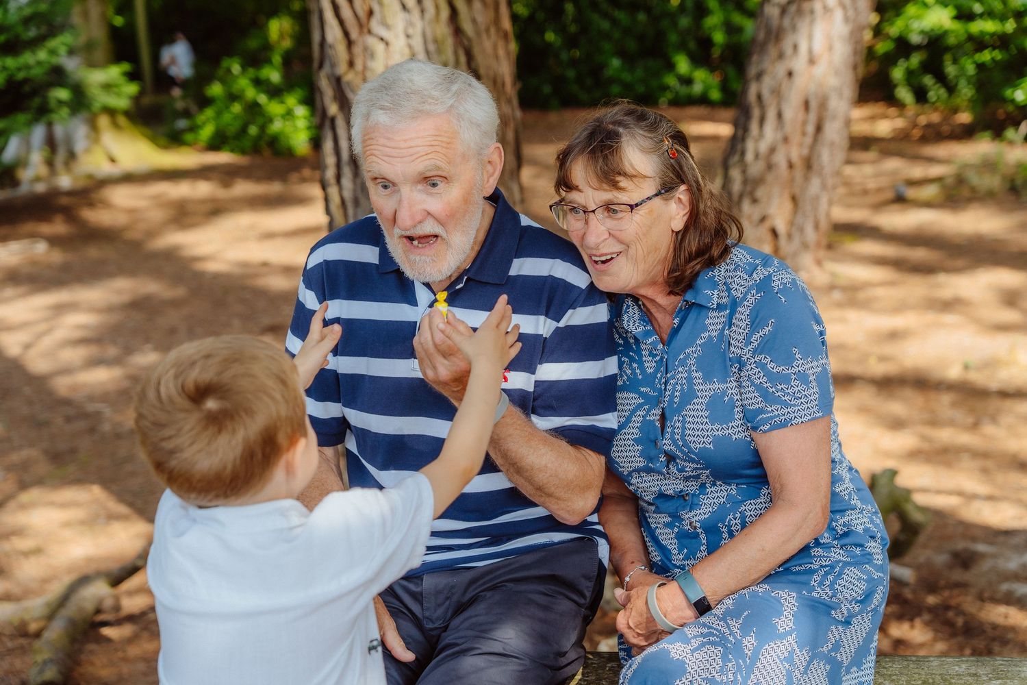 Grandparents joyfully interacting with a young child outdoors, sharing a playful moment among trees.