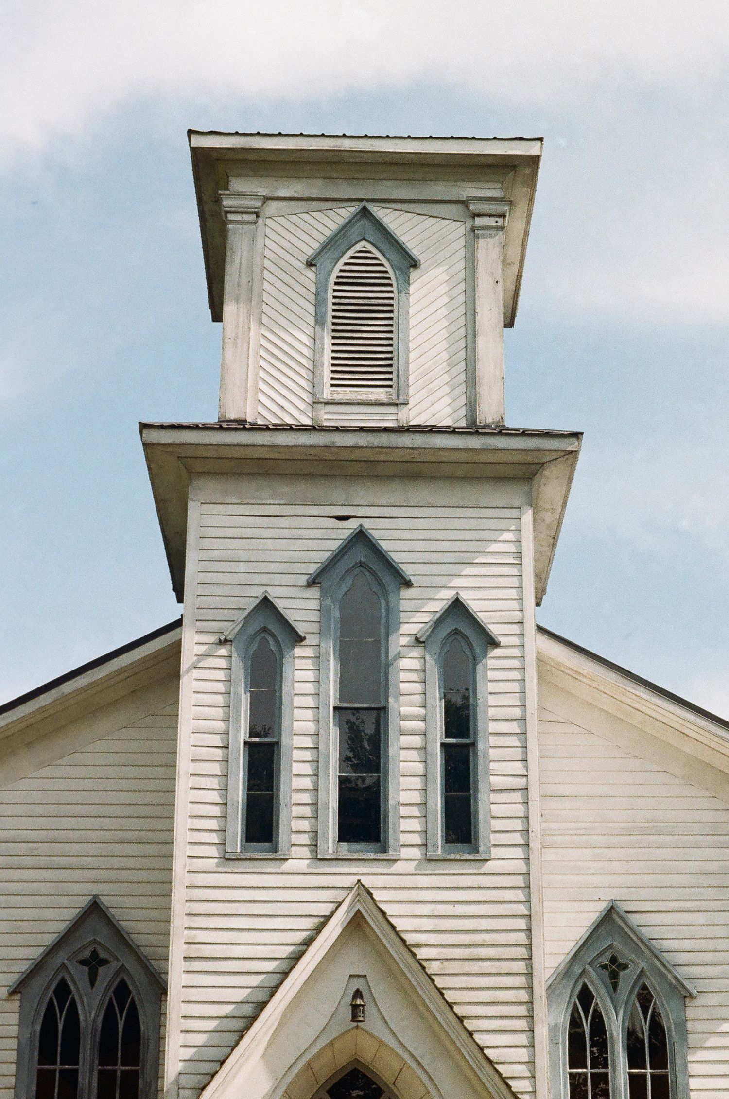 White wooden church steeple with Gothic arch windows against a cloudy sky. Cranberry Creek Gardens Ontario