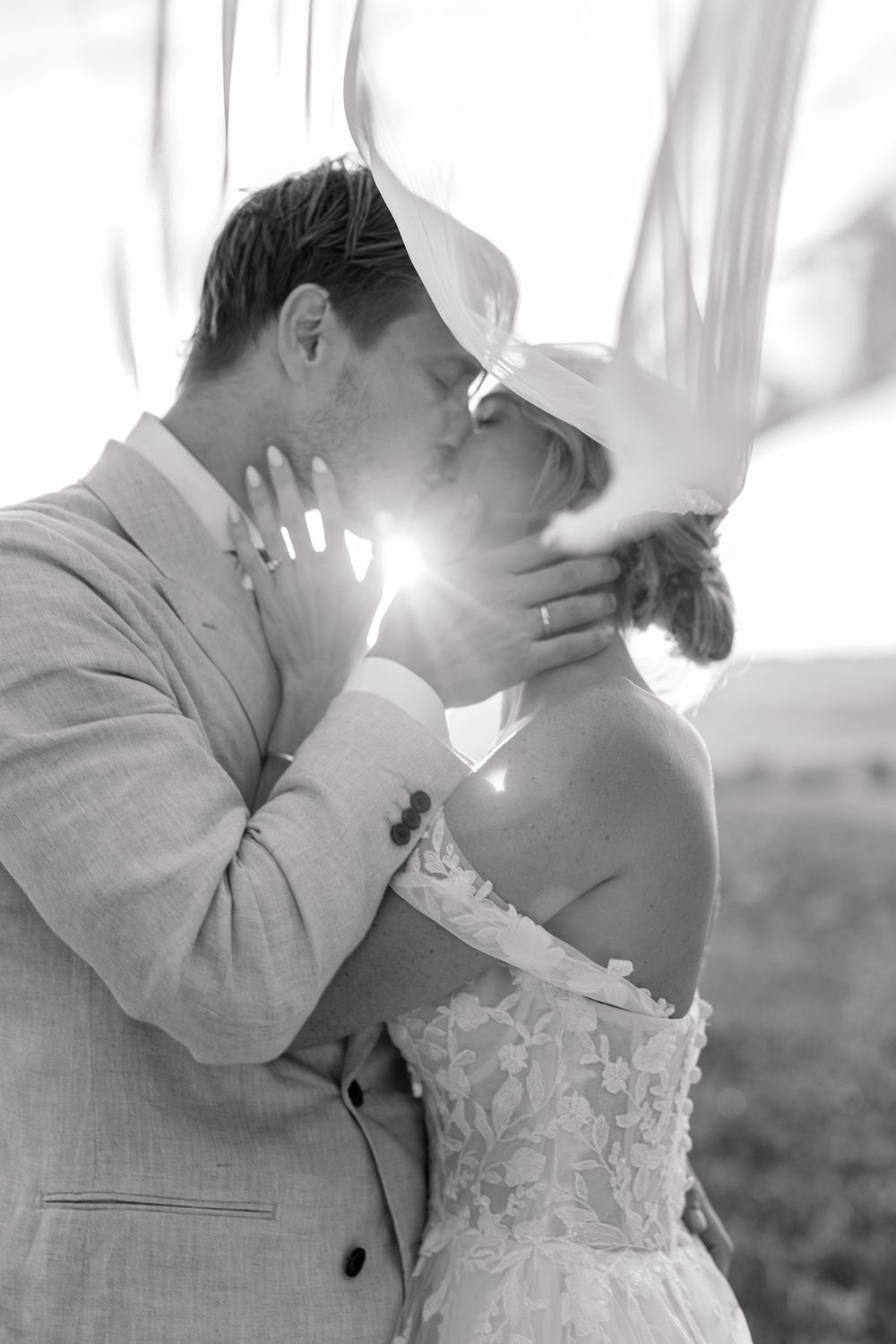 Black and white photo of a bride and groom sharing a romantic kiss, with soft light glowing between them on their wedding day.