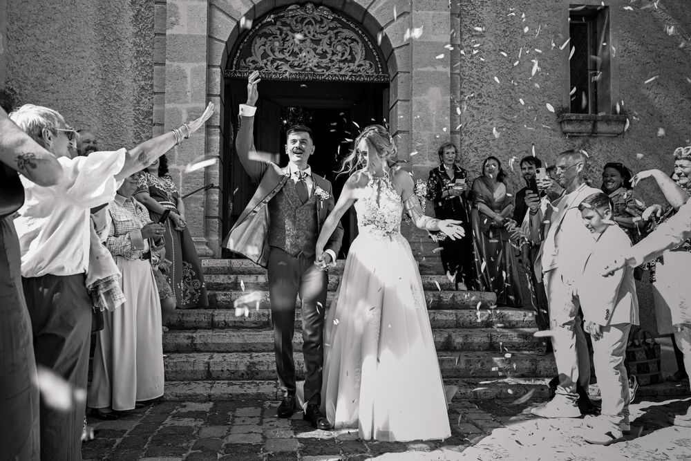 Bride and groom exit church amid confetti shower, guests celebrating joyful wedding ceremony outdoors.