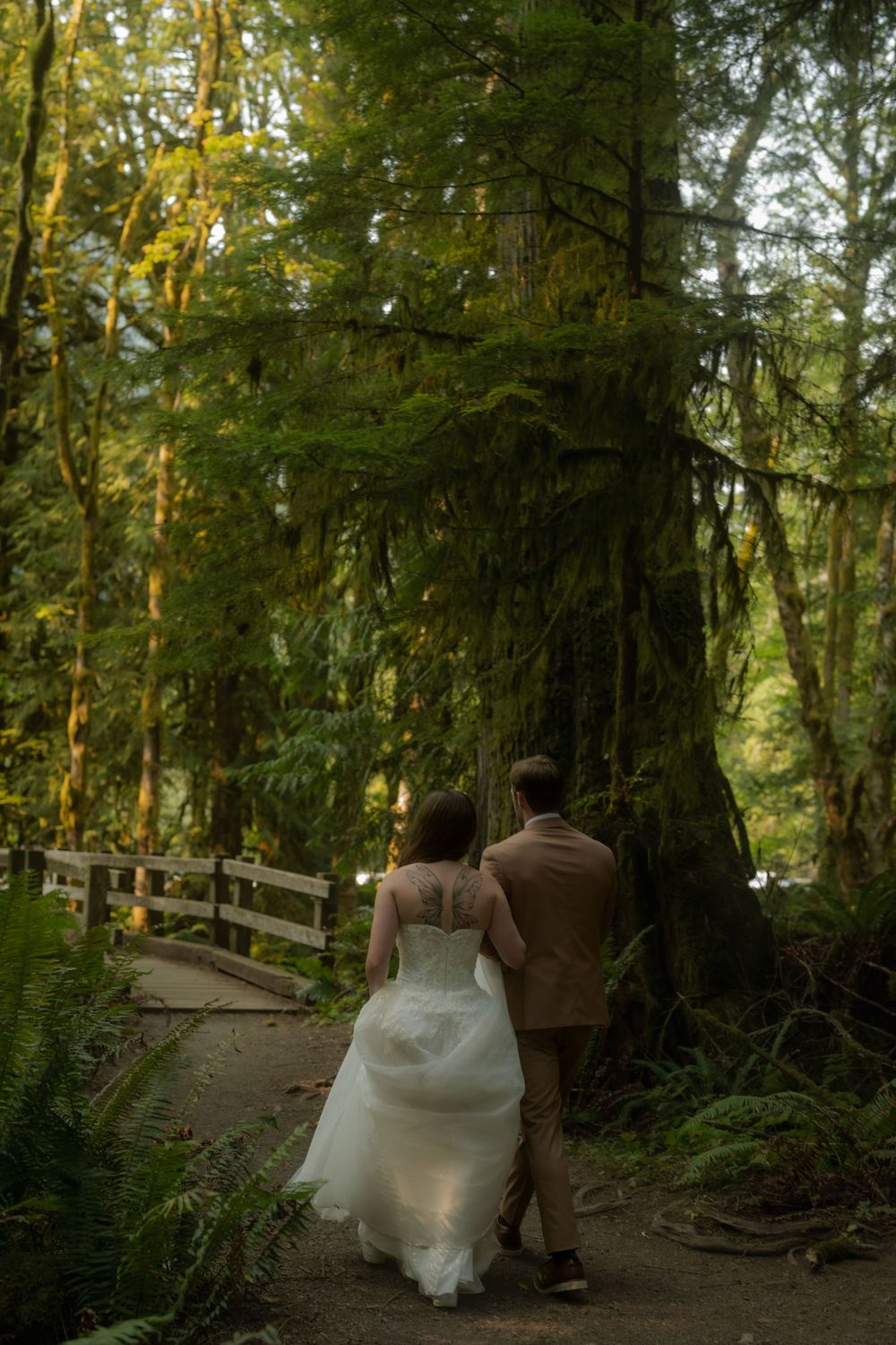 A bride and groom walk hand-in-hand through a lush green forest on their wedding day.