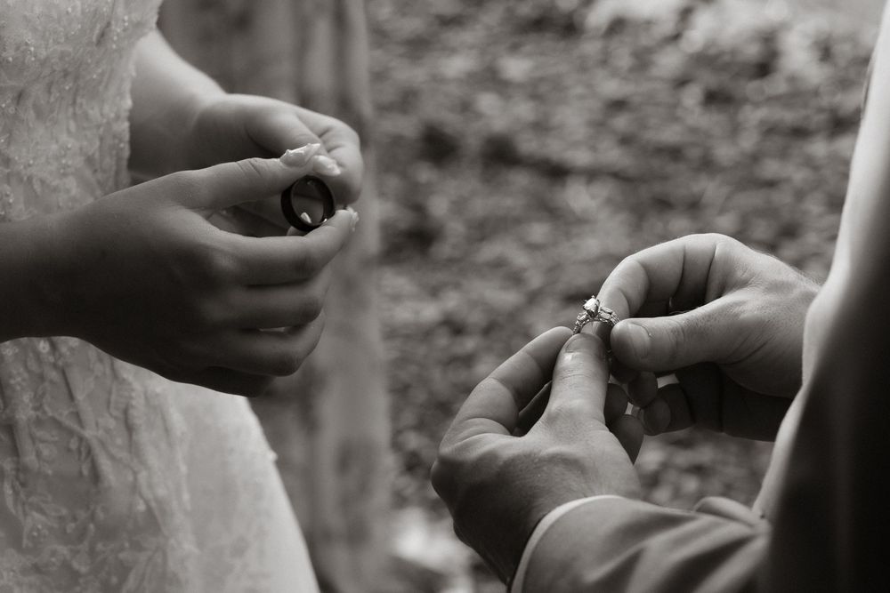 Black and white photo of hands exchanging wedding rings during a marriage ceremony.