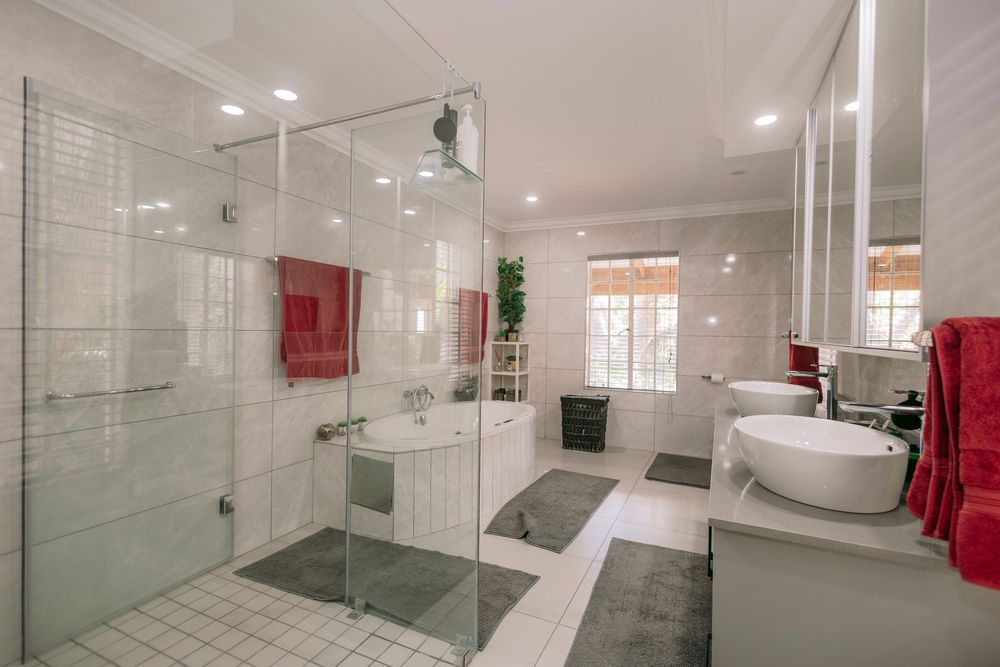 Modern luxury bathroom featuring glass shower enclosure, dual vessel sinks, white tiles, and red accent towels.