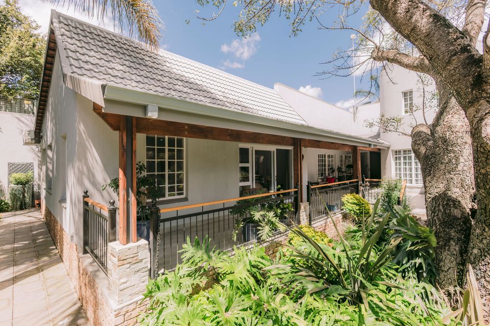 Charming cottage-style home with white walls, timber accents, metal roof, and lush garden greenery under a blue sky.