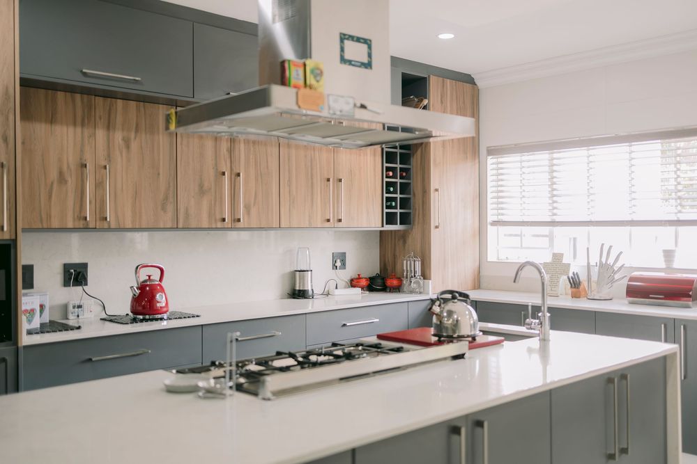 Modern kitchen with gray cabinets, wood accents, stainless steel hood, gas cooktop island, and red kettle accents.
