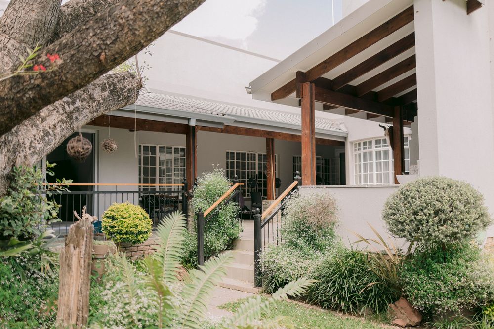 Charming house exterior with lush garden, wooden pergola, and manicured shrubs lining a pathway to the entrance.