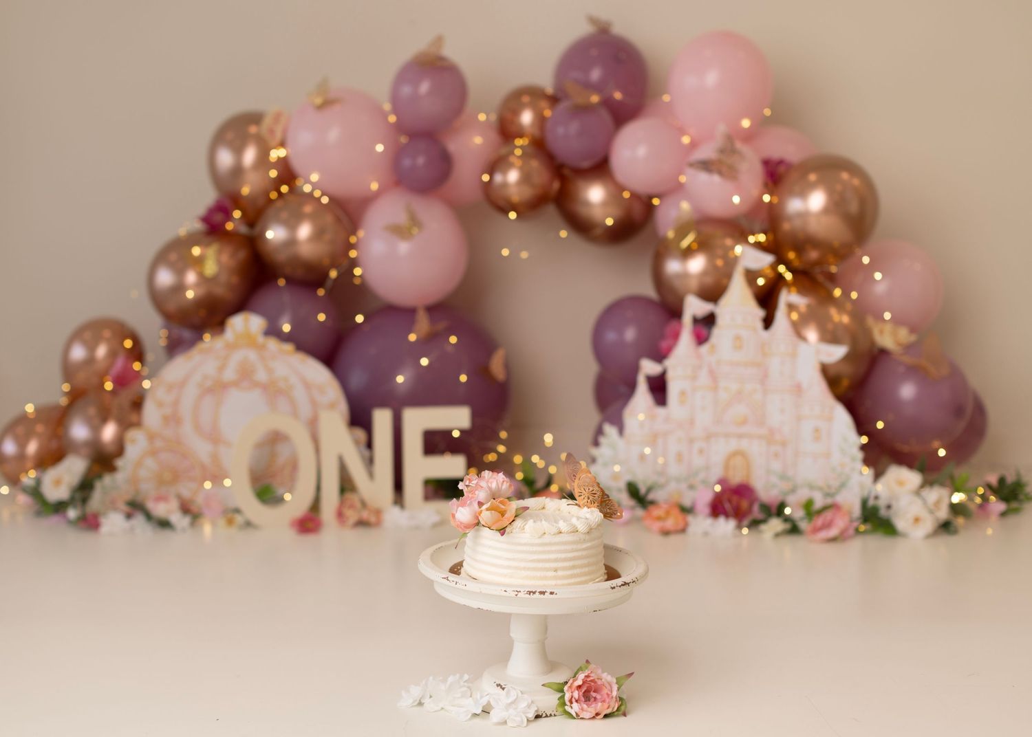 Pink and gold balloon arch with ONE sign and princess castle cake for a first birthday party celebration.
