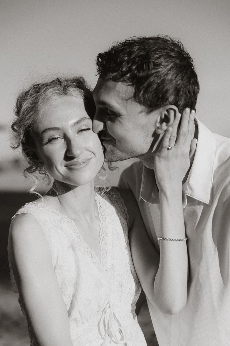 Black and white photo of a groom whispering in his smiling bride's ear on their wedding day.